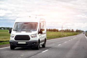 White commercial cargo van traveling on rural asphalt road during daytime under overcast sky, transportation of goods and people between cities, delivery vehicle moving
