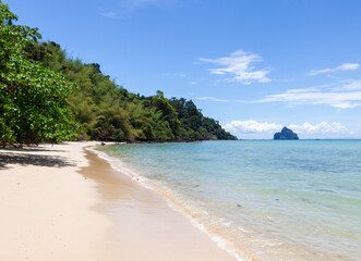 Obraz premium Koh Kradan island beach in Thailand. Tropical coastline with clear turquoise water. Lush greenery and rocky formations near blue ocean.
