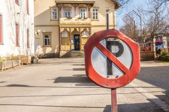 Verbeultes Verkehrsschild Parkverbot vor leerem Platz mit Geb&auml;ude im funktionalen Industriebaustil mit Sprossenfenstern,  Holzveranda und halbrundem Treppenaufgang im Seitenlicht  in N&uuml;rtingen. 