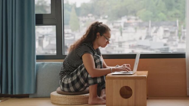Travel work session. Business traveler using laptop with city view and documents spread out. Professional engaged in email editing while seated at wooden table overlooking urban skyline