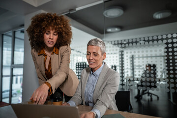 Fototapeta premium Diverse businesswomen collaborating on project using laptop in modern office