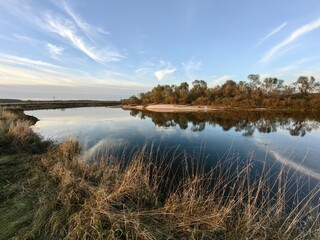 Autumn landscape with a river, blue sky and wild grasses.