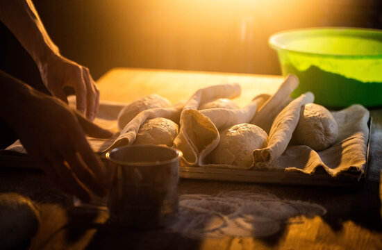 Hands shaping fresh artisan bread dough on rustic table with flour, golden light illuminating preparation of natural loaves, embodying baking process and culinary craft