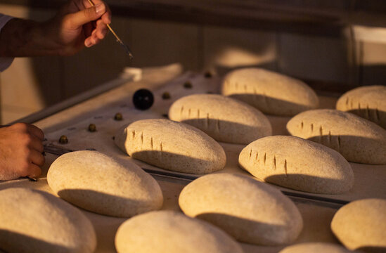 Human hands prepare bread dough loaves for baking process at commercial bakery facility. Manual scoring of dough prior to oven placement. Traditional bread making technique.