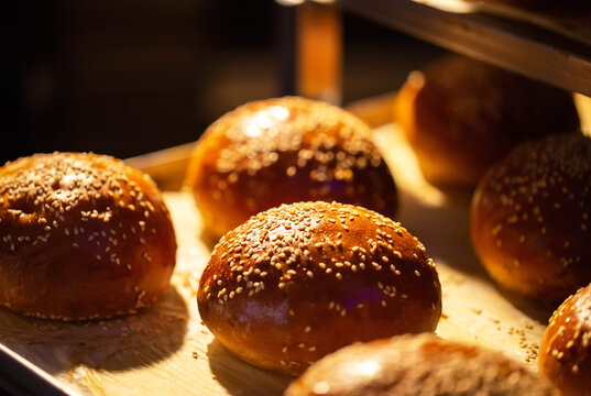 Warm golden brown brioche style buns with sesame seeds fresh from oven display. Delicious baked goods ready for consumption or preparation.
