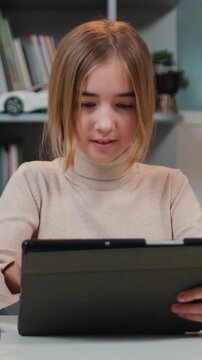 Close up pretty 10s girl sitting in home classroom with tablet device, studying, play video game, use modern wireless tech. Kid safety on internet concept