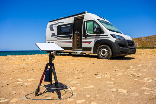 Camper van parked on remote beach during free camping on Limnos Island, Greece. Starlink satellite internet dish set up for digital nomad remote work. Vanlife road trip with motorhome by Mediterranean