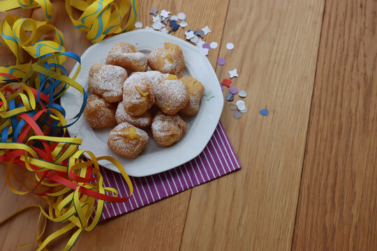 Traditional italian fritters filled with cream called Frittelle on a plate on wooden table with colorful paper streamers and confetti with copy space