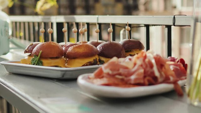Close-up of snacks on a cafe terrace, catering of mini burgers on skewers, buffet table at a wedding or birthday party. Trays with appetizers of meat, fruit, grapes, cheese and ham. Slow motion.