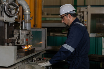 Industrial worker grinding metal on machine in factory workshop, wearing hard hat, safety glasses...