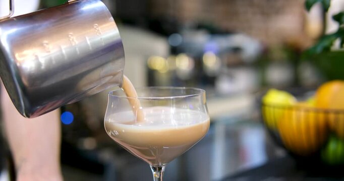 Barista pouring cocktail Ice coffee latte with cream being poured into it showing the texture and refreshing look of the drink, with a clean background.