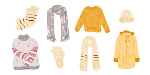 Collection of winter clothing items including socks, scarves, sweaters, gloves, and a coat in various colors and patterns arranged on a white background © Olena