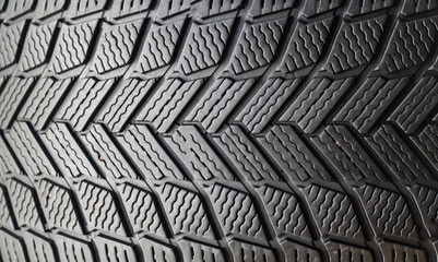 Fototapeta premium Winter friction tires with tread pattern or close-up texture. The concept of driving safety in winter on a slippery road. Winter studless car tires on a black background in close-up. 
