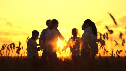 Fototapeta premium Happy mom dad children dancing in meadow sunset, slow motion. Family, mother father kids happily dance on grass, enjoying nature at sunset. Family party outdoor. Parents dad mom, daughter son picnic