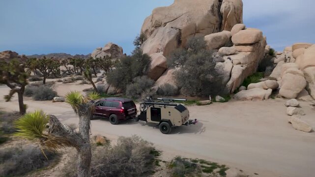 Explore an SUV pulling a teardrop camper trailer in Joshua Tree National Park in California with bikes, traveling through the desert landscape.