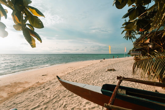 View of a vibrant beach scene with a grounded boat, framed by lush foliage against the backdrop of the serene sea, Badian, Central Visayas, Philippines.