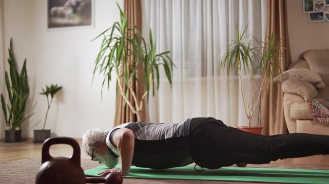 Elderly man with white beard in sports uniform performs power exercises on floor