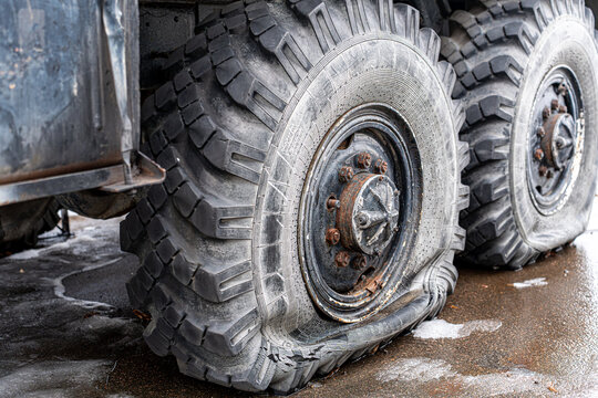 View of a flat tire on a heavy-duty truck, sitting forlornly on the wet asphalt, its robust tread deflated against the unforgiving ground, Kyiv, Ukraine.