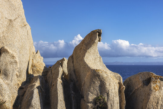 View of sun-kissed granite rocks sculpted by time and the sea against a backdrop of azure sky and distant horizon, Capo Testa, Sardegna, Italy.