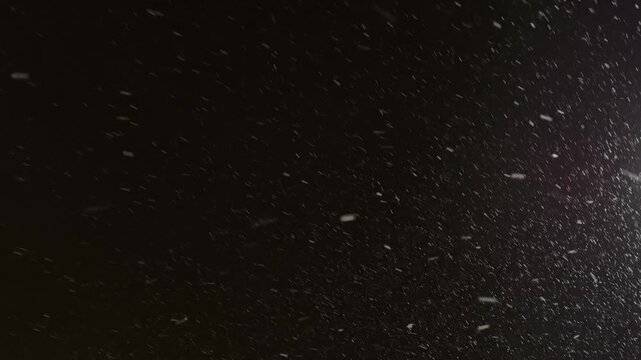Street light illuminating falling snow during snowstorm at night. Realistic falling snow effect against a dark night sky, ideal for compositing winter scenes, creating a serene and magical atmosphere.