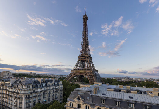 View of the Eiffel Tower soaring above Parisian rooftops under a soft, pastel sky, a captivating blend of architectural grandeur and urban charm, Paris, Ile-de-France, France.