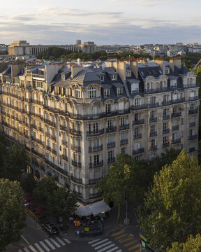 View of an elegant Parisian building basks in the warm glow of the setting sun, its classic architecture standing proudly against the lush green canopy, Paris, Ile-de-France, France.
