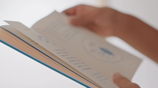 Closeup hands reading hotel guidebook in bright room, hotel guest flipping clean pages, delicate manicure, slow deliberate turns, soft natural light, quiet refined atmosphere, focus on cover edge