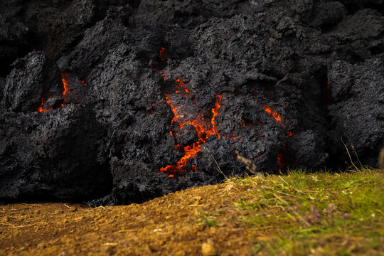 View of molten lava cracks through the dark, textured volcanic rock, contrasting with the green grass, Grindavik, Grindavikurbaer, Iceland.