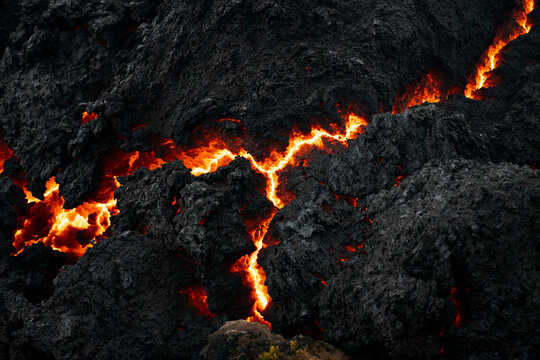 View of molten lava snakes through jagged black volcanic rock, a fiery river against the earth's dark crust, a dance of destruction and creation, Grindavik, Iceland.