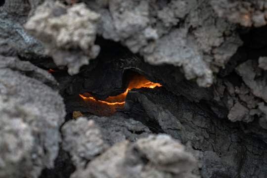 View of a fiery glow peeks through the jagged, dark volcanic rock, a stark contrast of intense heat and solid earth, Grindavik, Grindavikurbaer, Iceland.