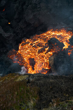 View of molten lava flowing like a fiery river against a backdrop of black volcanic rock, creating a stark contrast of destruction and awe, Grindavik, Iceland.