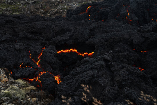 View of fiery orange lava flows creep across the stark black volcanic rock, a raw display of geothermal power and destruction, Grindavik, Iceland.