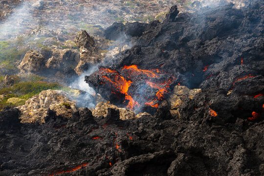 View of molten lava flowing like fire through a stark, blackened landscape, juxtaposed against patches of resilient green moss, Grindavik, Iceland.