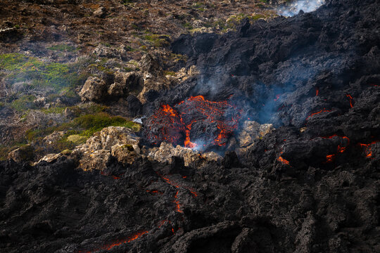 View of molten lava flows like fiery rivers through jagged, black volcanic rock, contrasting with patches of green moss, Grindavik, Grindavikurbaer, Iceland.