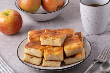 Freshly baked apple squares on a plate with apples in a bowl at a kitchen table during