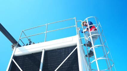 Fototapeta premium Young man engineer climbing a metal ladder to inspect industrial equipment