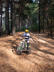 Motocross rider on motorcycle driving through forest trails. Man in protective gear riding bike on rough terrain. Off-road motorbike adventure in woodland. Extreme sport outdoor activity. © Olesia Basova