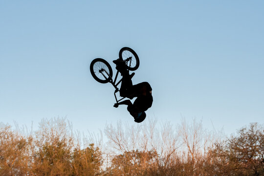 Persona a contraluz haciendo un salto en bicicleta.