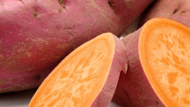 Freshly harvested sweet potatoes, whole and sliced, arranged against a clean white background.