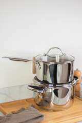Minimal stainless steel cookware set with pot and saucepan on wooden board in bright modern kitchen environment.