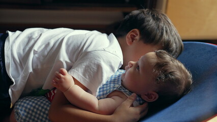 Young boy lying down embracing baby sibling, affectionate sibling connection, warmth and love, gentle family moment, childhood bond, close and tender interaction