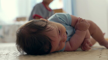 Baby lying on mat, gazing at camera, soft expression, warm home atmosphere, early childhood development, calm moment, infant curiosity, peaceful indoor setting