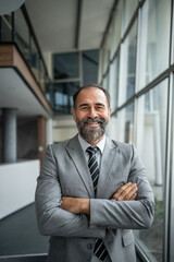 Fototapeta premium Senior businessman smiling with crossed arms in office corridor