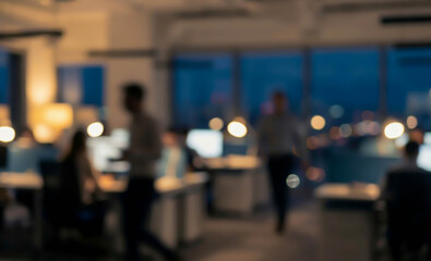 Blurred view of a modern office at night with workers engaged in tasks. Soft lighting creates a professional atmosphere with multiple computer screens visible.