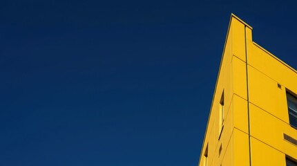 Minimalist architecture of a bright yellow building corner against a clear deep blue sky background