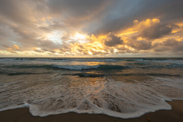 Obraz premium Dramatic ocean sunrise after storm with waves washing onto sandy beach