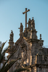 Fototapeta premium Baroque church rooftop with stone statues and a large cross, seagulls perched above, warm sunset light against a clear blue sky.