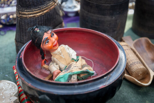 A vintage puppet doll resting inside a black and red lacquered wooden bowl.