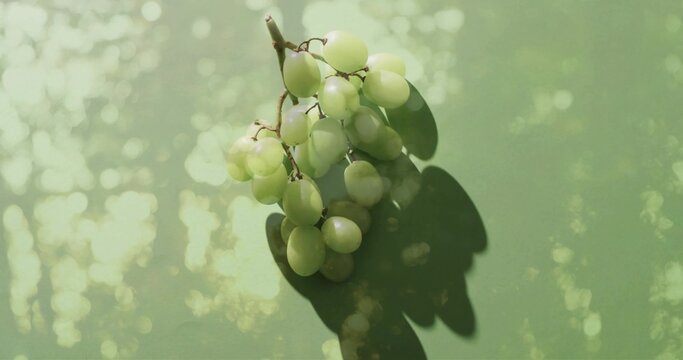 Resting pale green grape cluster casting shadow on table, short woody stem amid bokeh highlights