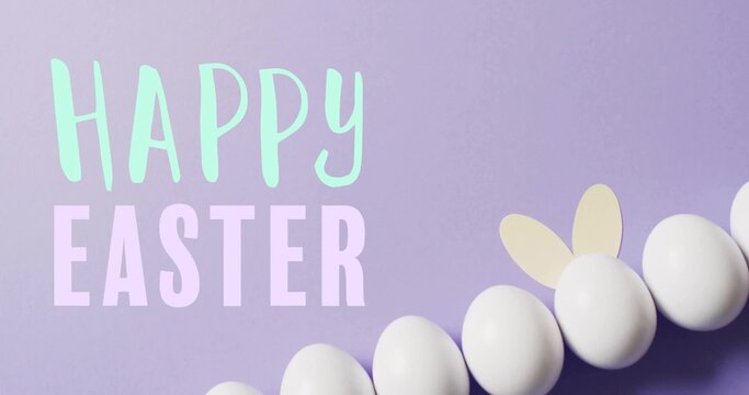Displaying white eggs with bunny ears on pastel lavender flat-lay, showing HAPPY EASTER letters